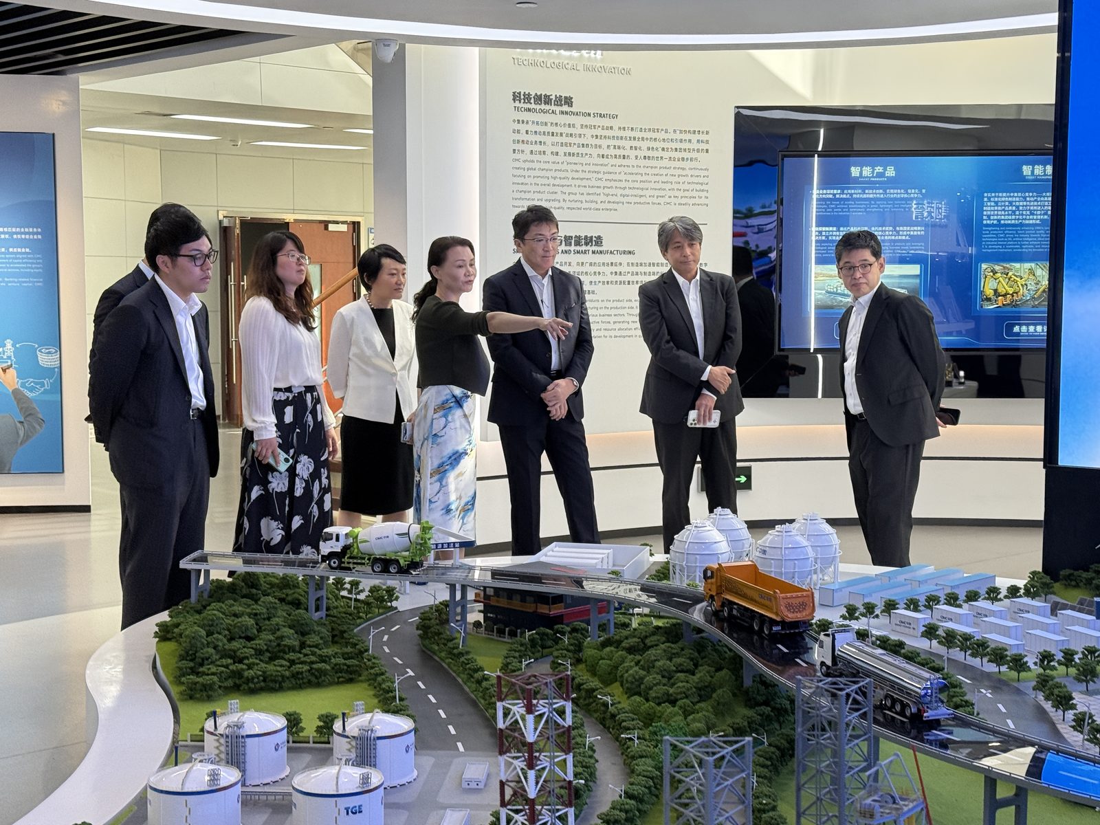 Mitsui & Co. delegation and CIMC ENRIC team at the exhibition-hall sand table showing the full gas chain from storage terminals to truck and rail logistics